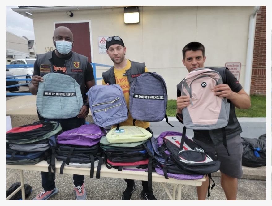 Three volunteers holding backpacks at a back-to-school giveaway event